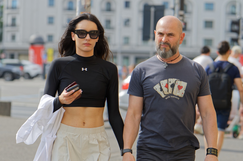 26 - Couple walking in an urban setting, with woman wearing a black Under Armour long-sleeve crop top paired with beige cargo pants